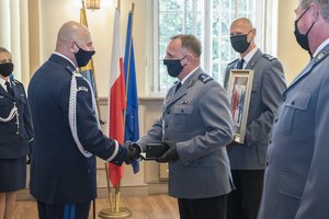 3 policjanci gratulują generałowi, jeden trzyma pamiątkowe zdjęcie w ramce jako prezent